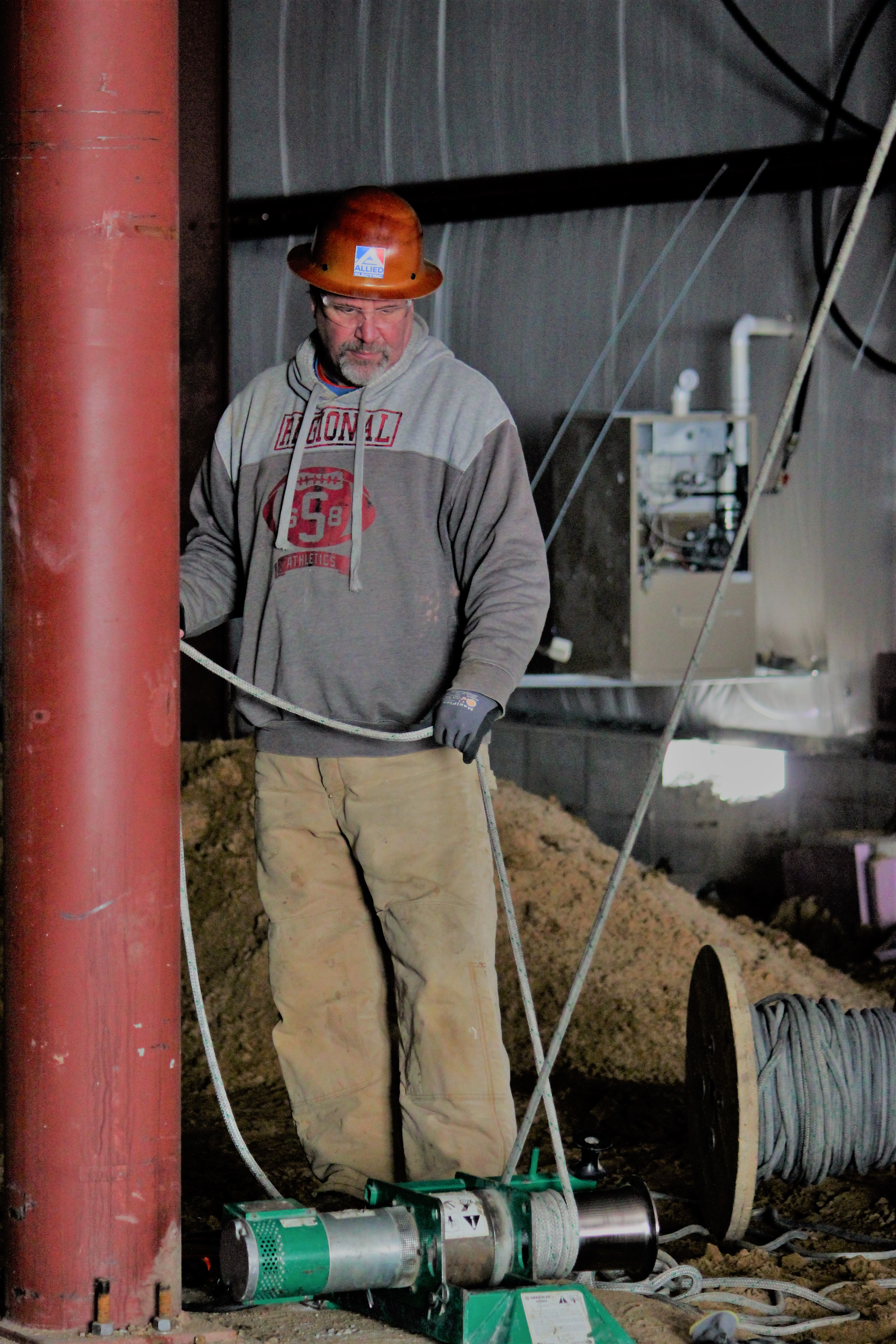 Allied Electric worker in orange hard hat operating electrical equipment in underground construction area
