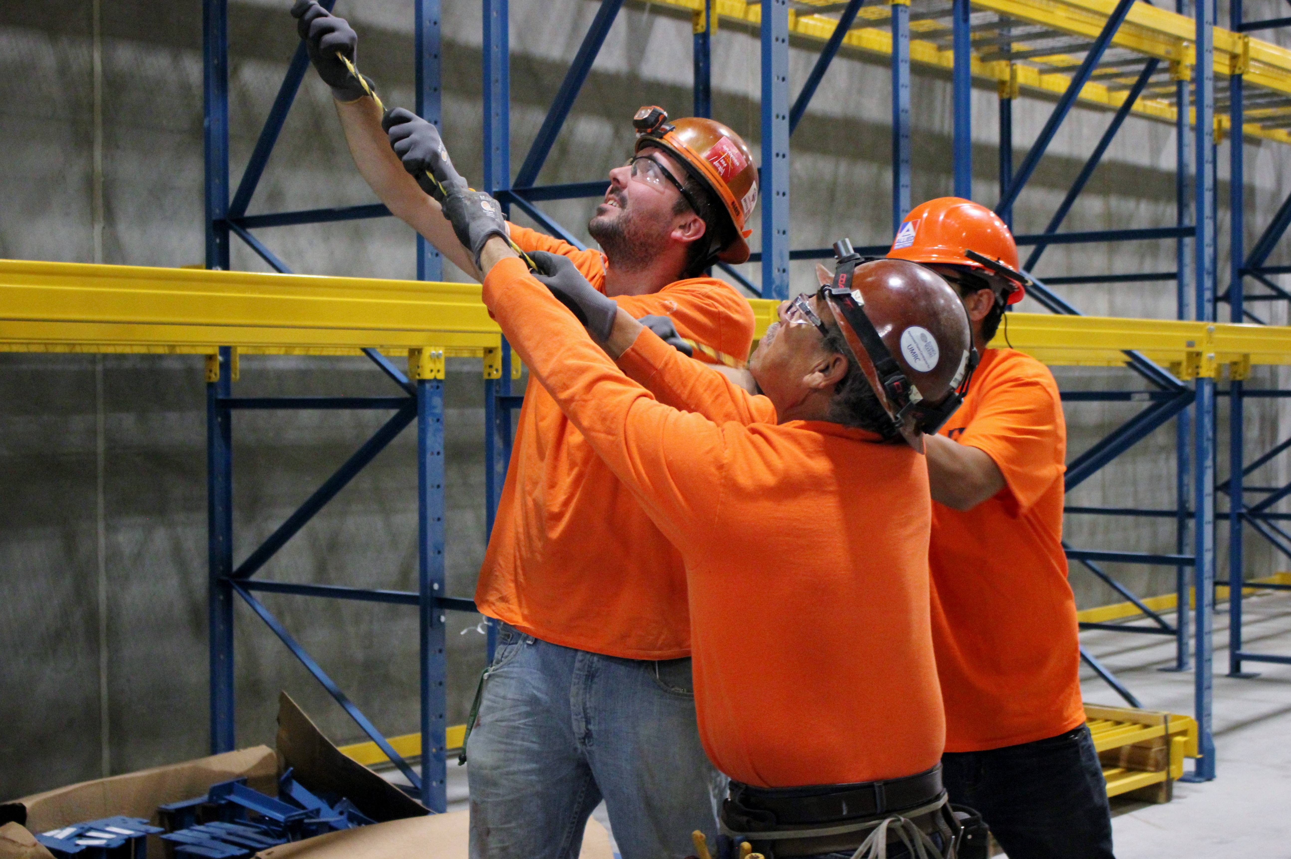 Allied Electric workers in orange safety gear collaborating on electrical installation in industrial warehouse