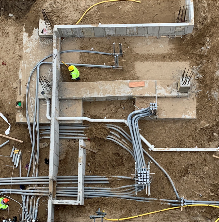 Electrical conduit installation at construction site with workers in safety gear